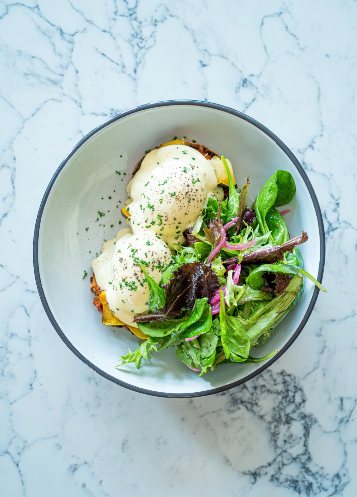 two poached eggs under hollandaise with a dressed green salad